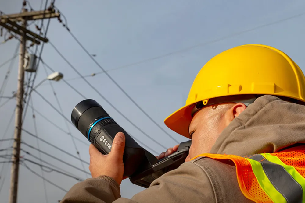 Técnico inspecionando linhas aéreas com a FLIR T8xx pelo visor ocular sob luz solar forte